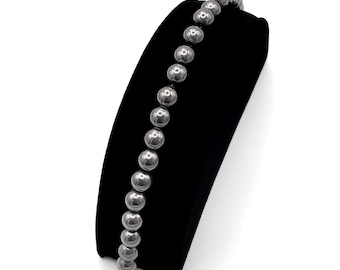 May include: A silver beaded bracelet with a clasp closure. The bracelet is displayed on a black velvet stand.