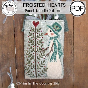 May include: A punch needle pattern featuring a snowman with a green hat and scarf standing next to a small tree with red berries. The pattern is titled "Frosted Hearts" and is by Prim In The Country.