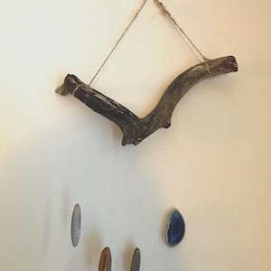 May include: A wooden branch with twine hanging from a hook on a white wall.  Four agate slices hang from the branch, two are brown and two are blue.