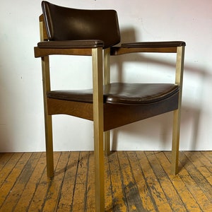 May include: A brown leather chair with a wooden seat and gold metal legs. The chair has a padded back and armrests.