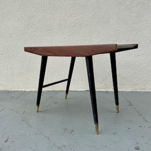 May include: A mid-century modern side table with a dark wood top and black legs with gold accents.