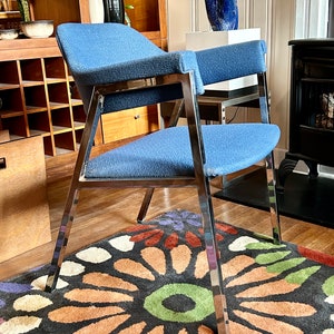 May include: A blue upholstered chair with a chrome frame sits on a colorful rug with a floral pattern. The chair has a high back and arms.