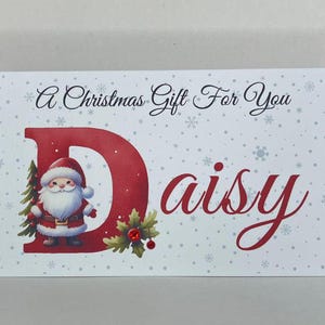 May include: A rectangular Christmas gift card with a festive design. The card features a red letter "D" with a Santa Claus illustration, the name "Daisy" in cursive, and the text "A Christmas Gift For You". Snowflakes are scattered across the white background.