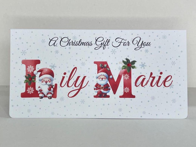May include: A rectangular Christmas gift card with the text "A Christmas Gift For You" and the name "Lily Marie". The letters are red and decorated with Santa Claus illustrations and snowflakes.