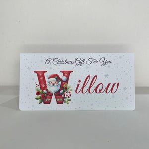 May include: A rectangular Christmas gift card with a festive design. The card features the text "A Christmas Gift For You" and the name "Willow" in red script. The letter "W" is decorated with Santa Claus.