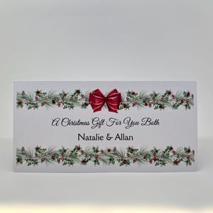 May include: A rectangular Christmas gift card with a red bow and festive greenery. The card reads "A Christmas Gift For You Both" with the names "Natalie & Allan" below.