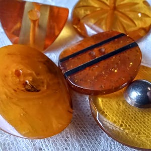 May include: A collection of vintage orange and amber-colored buttons in various shapes and designs. Some buttons have stripes, while others have a textured or carved appearance. The buttons are made of a translucent material.