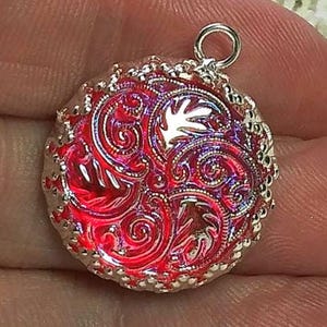 May include: A silver pendant with a red, iridescent, circular charm featuring a detailed floral design.