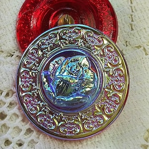 May include: A vintage iridescent glass button with a raised rose design and a gold-colored border. The button is red and has a blue and green iridescent sheen.