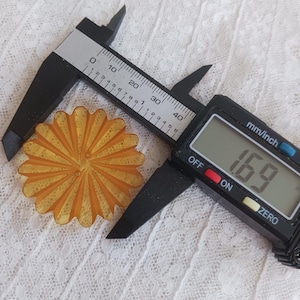 May include: An orange, flower-shaped object is measured with a digital caliper. The caliper displays a measurement of 1.69 mm. The object has a detailed, sunburst design.