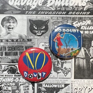 May include: Two round No Doubt band pins. The first pin is red with a blue and yellow "NO" and a black "DOUBT". The second pin is blue with a white "NO DOUBT" and a picture of a woman in a red dress standing in a field.