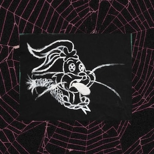 May include: A black square with a white chalk drawing of a cartoonish rabbit-like creature with its tongue out. The background is a spiderweb pattern in dark pink.