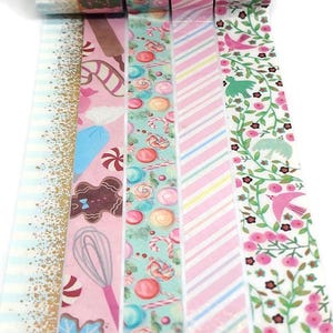 May include: A set of six decorative washi tapes featuring a variety of designs, including candy canes, gingerbread, and floral patterns. The tapes are pink, blue, green, and white.