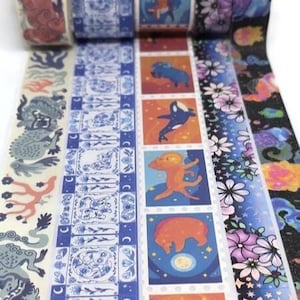 May include: Decorative washi tape rolls featuring various designs. The rolls include patterns with mythical creatures, floral arrangements, and celestial themes. The color palette includes shades of blue, orange, purple, and black. The tape is ideal for scrapbooking and crafting.