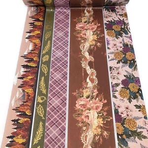 May include: Decorative washi tape rolls featuring various designs. The rolls include patterns of autumn landscapes, gold leaf accents, plaid, floral arrangements, and botanical prints. The color palette includes shades of brown, pink, green, and gold.