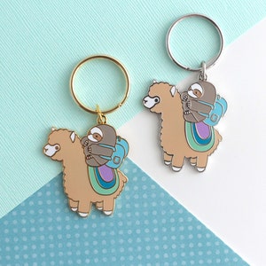 Two keychains of little grey sloths wearing a backpack and riding on top of a beige alpaca (or llama)