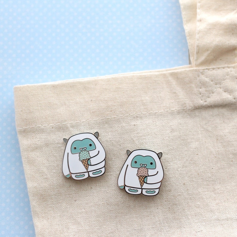 Two enamel pins of a white and blue yeti enjoying an ice cream, on a tote bag