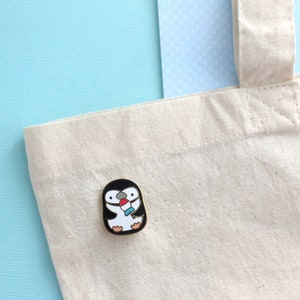 Tote bag decorated with an enamel pin of a chinstrap penguin enjoying a rocket fish ice pop