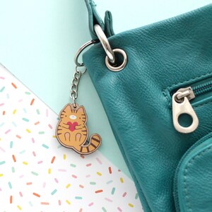 Wooden keychain of an orange tabby cat holding a heart attached on a green purse