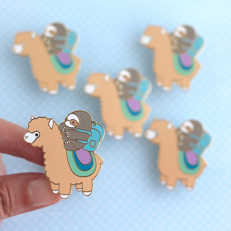 Hand showing large enamel pin of a sloth wearing a backpack and riding on top of an alpaca (or llama)