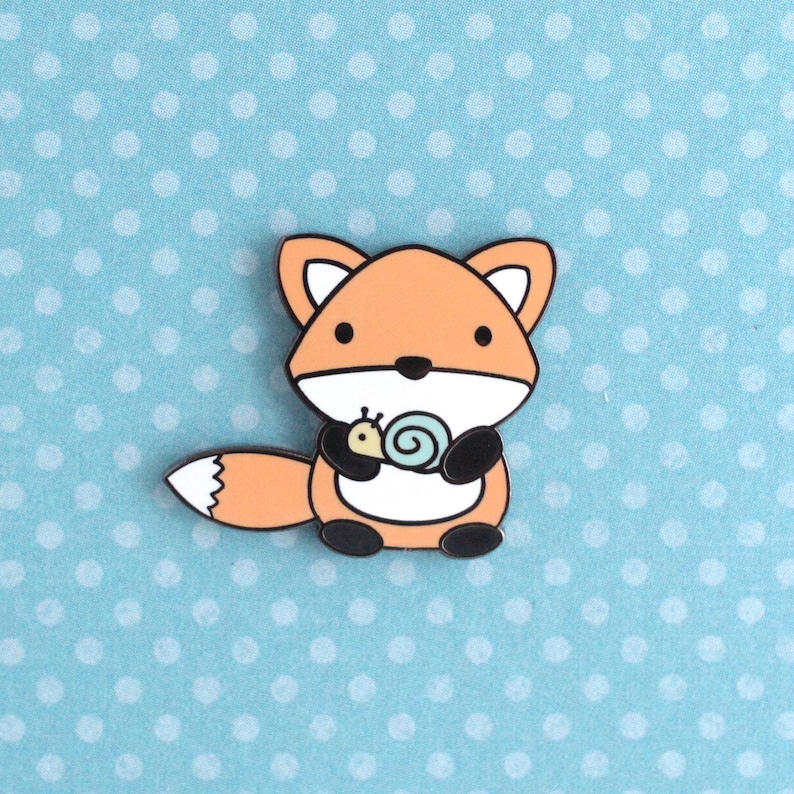 Enamel pin of a cartoon style orange fox holding a little snail