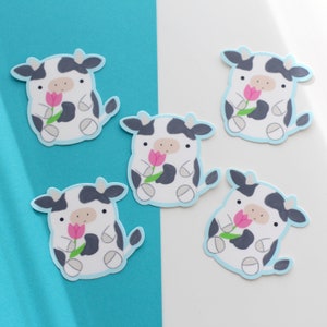 May include: Five black and white cow stickers with pink flowers. Each sticker has a light blue outline.