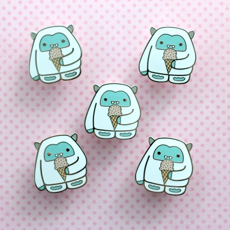 May include: Five white Yeti pins with blue accents, each holding a brown and white ice cream cone. The pins are on a pink background with white polka dots.