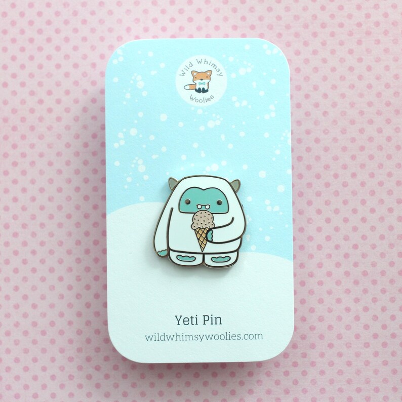 May include: A white Yeti with blue eyes and a brown ice cream cone in its hand. The Yeti is standing on a blue background with white snowflakes. The text "Wild Whimsy Woolies" and "Yeti Pin" are on the card.