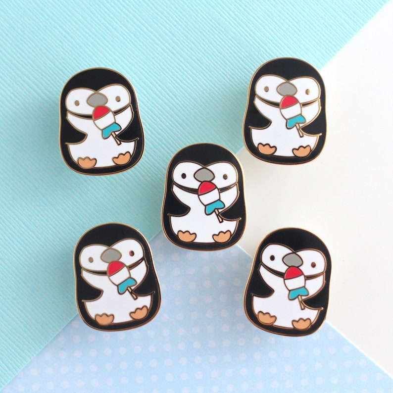 Five enamel pins of a chinstrap penguin enjoying a rocket fish ice pop