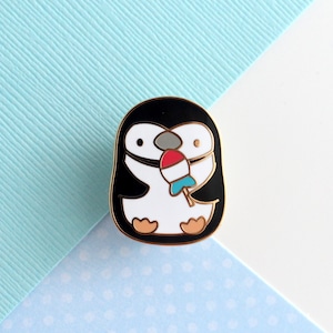 Enamel pin of a chinstrap penguin enjoying a rocket fish ice pop