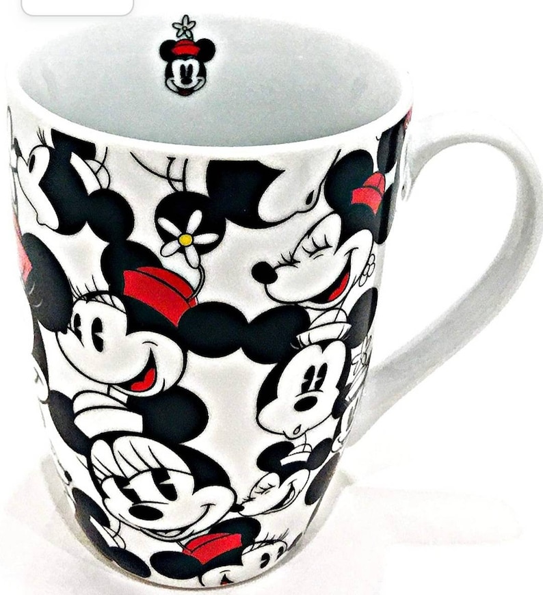 Puede incluir: Taza de cer&aacute;mica blanca con un patr&oacute;n repetido de caras de Minnie Mouse en negro, rojo y blanco. La taza tiene un asa curva y una peque&ntilde;a figura de Minnie Mouse dentro del borde. Un art&iacute;culo divertido y colorido para los fans de Disney.