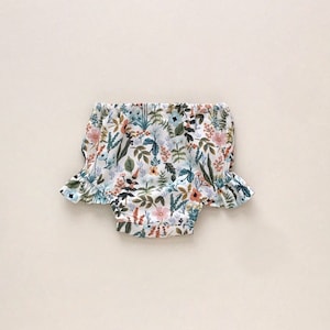 May include: White baby bloomers with a floral print featuring pink, blue, and green flowers and leaves.