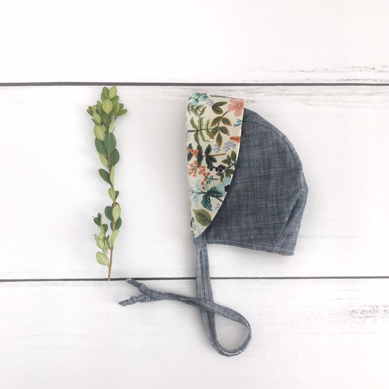 May include: A blue bonnet with a floral print lining. The bonnet has a tie that can be tied under the chin.