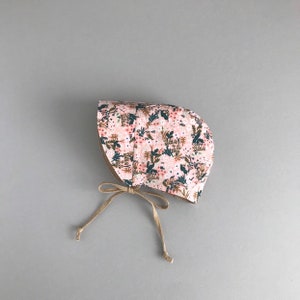 K&ouml;nnte beinhalten: Ein rosa Blumen-Sonnenhut mit brauner Schleife. Der Hut hat ein Blumenmuster mit rosa, gr&uuml;nen und braunen Blumen.