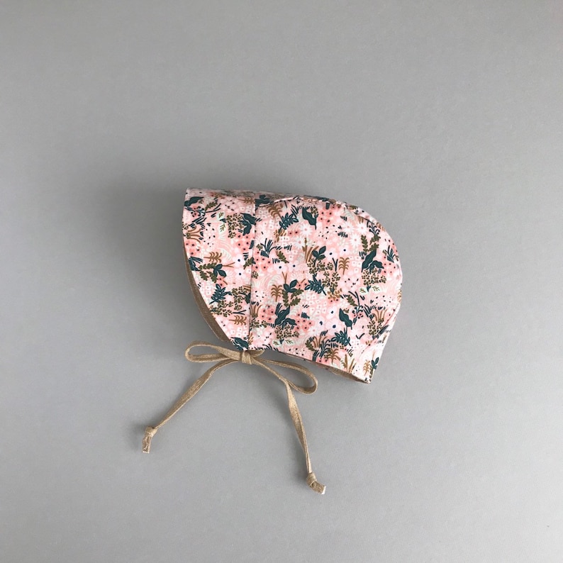 K&ouml;nnte beinhalten: Ein rosa Blumen-Sonnenhut mit brauner Schleife. Der Hut hat ein Blumenmuster mit rosa, gr&uuml;nen und braunen Blumen.