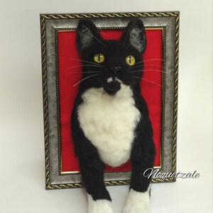 May include: A black and white cat with yellow eyes is peeking out of a silver frame with a red velvet background. The cat's paws are sticking out of the frame. The text "Noquetzale" is visible in the bottom right corner of the image.