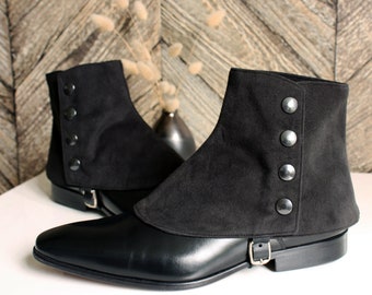 Puede incluir: Un par de botas de cuero negro con una polaina de ante negro con una fila de botones plateados. Las botas tienen una correa de hebilla en el lateral.