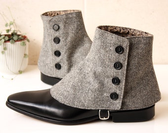 Puede incluir: Zapatos de cuero negro con polainas de tweed gris. Las polainas tienen cierre de botón y un patrón de espiga. Los zapatos tienen un detalle de hebilla y un tacón pequeño. Una planta en maceta blanca está en el fondo.