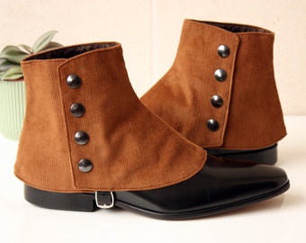 Puede incluir: Un par de polainas de pana marrón con bases de zapatos de cuero negro. Las polainas tienen tres botones oscuros y un cierre de hebilla. La pana es de un tono cálido y terroso, y los zapatos tienen un acabado brillante.