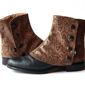 Peut inclure: Une paire de bottes en cuir marron avec un motif peau de serpent et des fermetures à boutons. Les bottes ont une semelle en cuir noir et une pointe pointue.