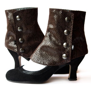 Könnte beinhalten: Ein Paar braune Lederstiefel mit Schlangenhautmuster und silbernen Knöpfen. Die Stiefel haben einen hohen Absatz und eine spitze Zehenpartie.