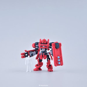 May include: A red and black articulated robot toy with a shield and a gun. The robot is standing on a white surface.