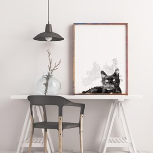 May include: Black and white watercolor painting of a cat with a gray background. The painting is framed in a brown frame and is hanging on a white wall above a white desk with a black chair.