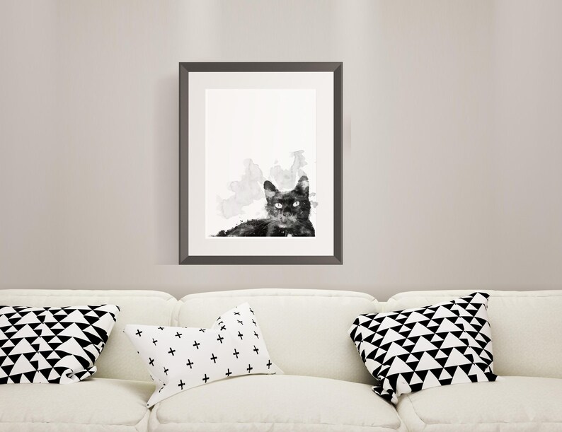 May include: Black and white watercolor painting of a cat with a white background. The cat is looking directly at the viewer. The painting is framed in a black frame.