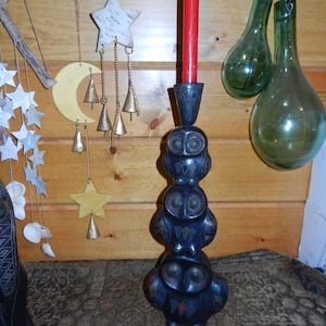 May include: A black wooden candle holder with three stacked owl figures. The owls have colorful accents and large eyes. A red candle is in the top owl's head.
