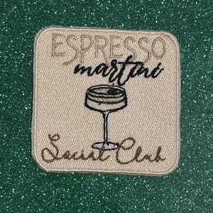 May include: Embroidered patch with the words "Espresso Martini Social Club" and a cocktail glass illustration. The patch is beige with brown and black stitching, set against a glittery green background.