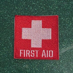 May include: A white ceramic mug with a black handle and the text "But First, Coffee" in a bold, black font. The mug is set against a blurred background, suggesting a cozy setting.