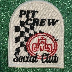 May include: White embroidered patch with the words "PIT CREW Social Club" in black lettering. A black and white checkered flag design is on the left side. A red circular emblem is on the right side.