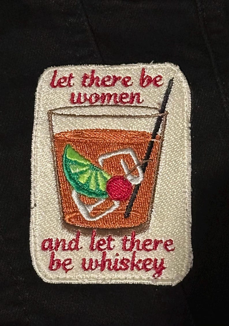 Pu&ograve; includere: Toppa ricamata con un design a cocktail. La toppa presenta una bevanda con una fetta di lime e ciliegia, una cannuccia e il testo "Let there be women and let there be whiskey" in rosso.