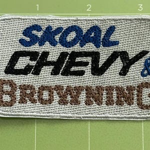 Pu&ograve; includere: Toppa ricamata con le parole "SKOAL CHEVY & BROWNING" in filo blu, nero e marrone su sfondo grigio chiaro. La toppa ha una forma rettangolare con angoli arrotondati e un bordo cucito.